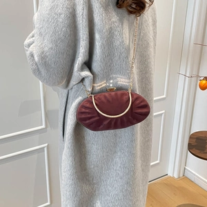 Detail of burgundy pleated evening clutch with gold handle worn over a grey plush coat