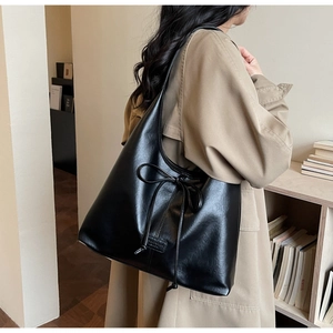 Black leather tote bag with bow detail worn by a model in a trench coat for work