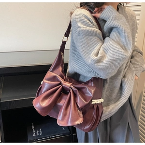 Close-up of wine red shoulder bag with large bow and white lace detail on a model
