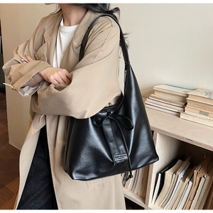 Detail of black glossy faux leather tote bag featuring a decorative drawstring bow and logo