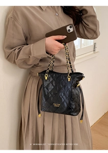 Close-up of black quilted leather bucket bag with gold chain strap and drawstring detail