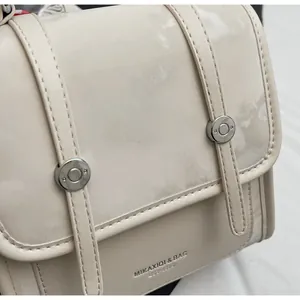 Close-up of cream shoulder bag featuring matte stitching and embossed brand logo detail
