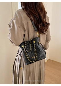 Detail of black quilted bucket bag with gold chain strap and drawstring closure