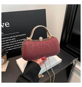 Close-up of burgundy velvet clutch featuring a gold curved handle and sparkling diamond clasp