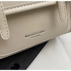 Macro detail of creamy white leather handbag with embossed silver logo and litchi texture