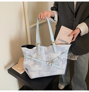 Close-up of textured tote bag with blue leather straps and metal buckle detail