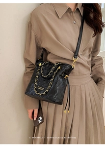Detail of black quilted bucket bag featuring a glossy finish and elegant gold chain strap