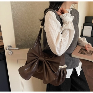 Macro detail of dark brown leather shoulder bag featuring large bow and lace trim