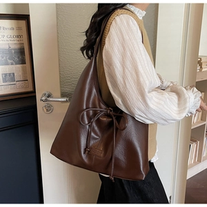 Detailed view of dark brown tote bag with drawstring bow and textured leather logo patch
