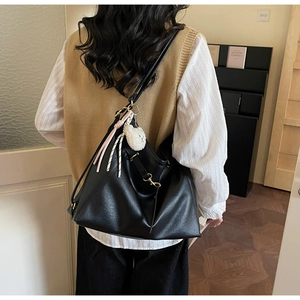 Side view of large black leather tote bag with fringe and white plush bear charm detail