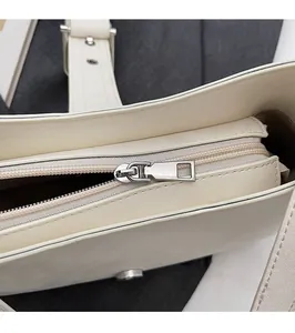 Gros plan sur la fermeture éclair argentée et les coutures d'un sac à main beige crème