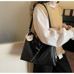Detail of black faux leather tote bag featuring a cute white plush bear pendant and scarf