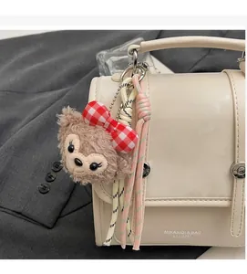 Close-up of ShellieMay plush bear charm hanging on a cream leather backpack handle