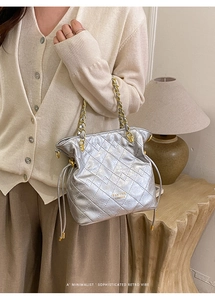 Close-up of a silver quilted bucket bag with a gold chain strap on a cream cardigan