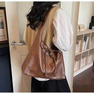 Detail of a brown tote bag featuring a leather bow and a branded logo patch