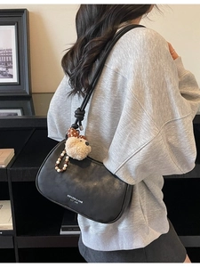 Chic black half-moon shoulder bag with plush bear charm and minimalist logo print