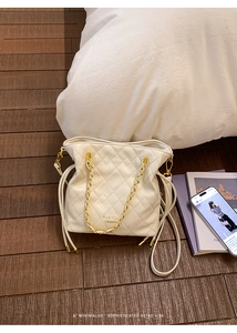 Close-up of beige quilted bucket bag with gold chain strap and drawstring closure