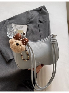 Minimalist light blue dumpling shoulder bag with plush bear charm on grey blazer