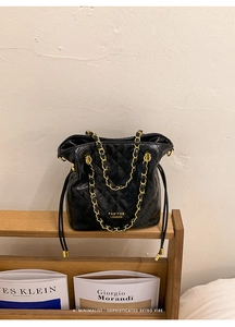 Detail of black quilted bucket bag featuring gold chain strap and logo on display stand