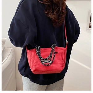 Detail of red checkered crossbody bag with woven rope handles and a fashion label