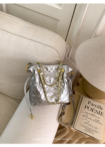 Detail of silver quilted bucket bag with gold chain strap on a beige sofa