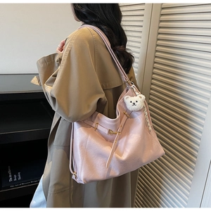 Close-up of pink oversized faux leather tote with plush bear pendant on khaki trench coat