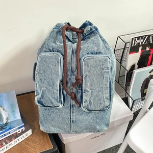 Detail of light blue denim backpack featuring thick brown cotton drawstrings and front pockets