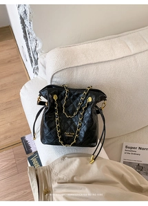 Detail of black quilted bucket bag with gold chain strap and logo on a beige sofa