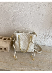 Close-up of cream quilted bucket bag with gold chain strap and drawstring closure