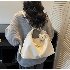 Detail of cream white leather tote bag with soft plush bear charm and golden buckle