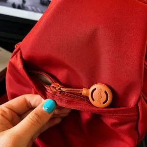 Detail of red nylon backpack showing smooth zipper and brown rubber puller with logo