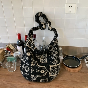 Dettaglio di una borsa tote in peluche a fantasia con manico a nodo su bancone in legno