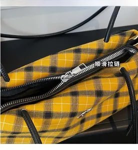 Close-up of the smooth metal zipper on the yellow plaid Boston handbag with woven texture