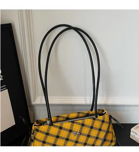 Detail of yellow plaid fabric handbag featuring a silver animal emblem and black leather strap