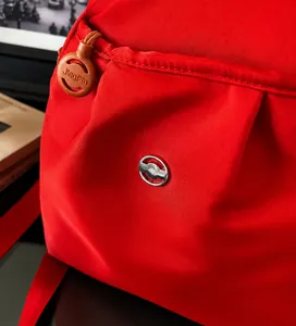 Macro shot of red Oxford fabric texture with brown zipper pull and metal logo detail