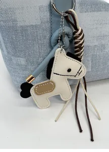 Détail d'un charme de cheval en cuir blanc avec corde tressée sur un sac à main bleu