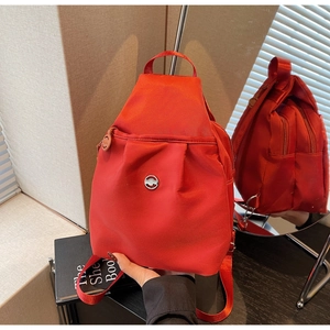 Detailansicht eines roten Nylon-Rucksacks mit mehreren Taschen und glänzendem Metall-Logo