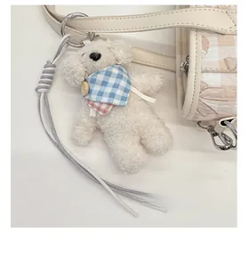 Gros plan d'un pendentif chiot en peluche blanche avec foulard à carreaux sur sac