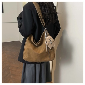 Détail d'un grand sac hobo marron avec charm ours porté à l'épaule par un mannequin
