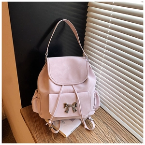 Detail of pink mini backpack with metal bow decoration and drawstring flap on wood surface