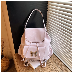 Close-up of pink faux leather backpack featuring a gold metal bow and drawstring detail