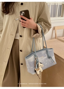 Détail du sac cabas minimaliste bleu et gris avec breloque cheval tenu par un mannequin