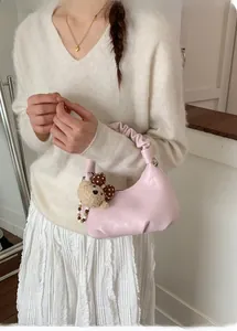 Detail of pink pleated handbag with cute bear charm and elegant pearl strap decoration