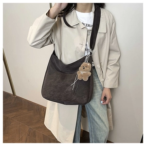 Detail view of large dark brown hobo shoulder bag with plush bear charm and wide strap