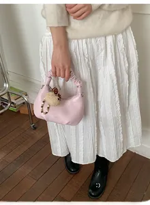 Pink leather chain bag with pleated handle and cute bear charm shown with white dress