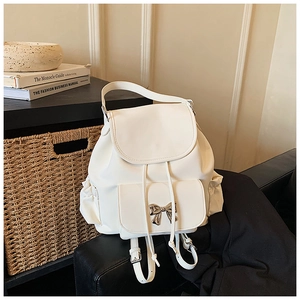 Detail of white leather backpack with elegant metal bow accent and flap closure design