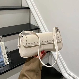Chic beige baguette bag with silver studs and adjustable strap on a minimalist stair