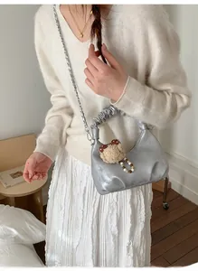Silver pleated cloud bag with metallic chain and cute bear charm shown in outdoor setting
