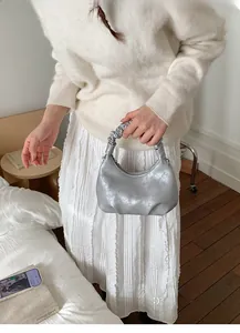 Silver pleated croissant bag with metallic finish shown on model in minimal interior