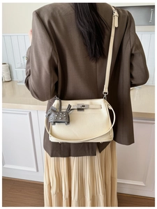 Vista cruzada de un bolso de cuero beige con cierre plateado y colgante de caballo